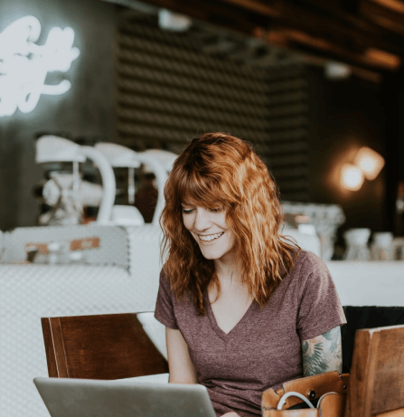 mulher em uma cafeteria, sorrindo enquanto utiliza o notebook